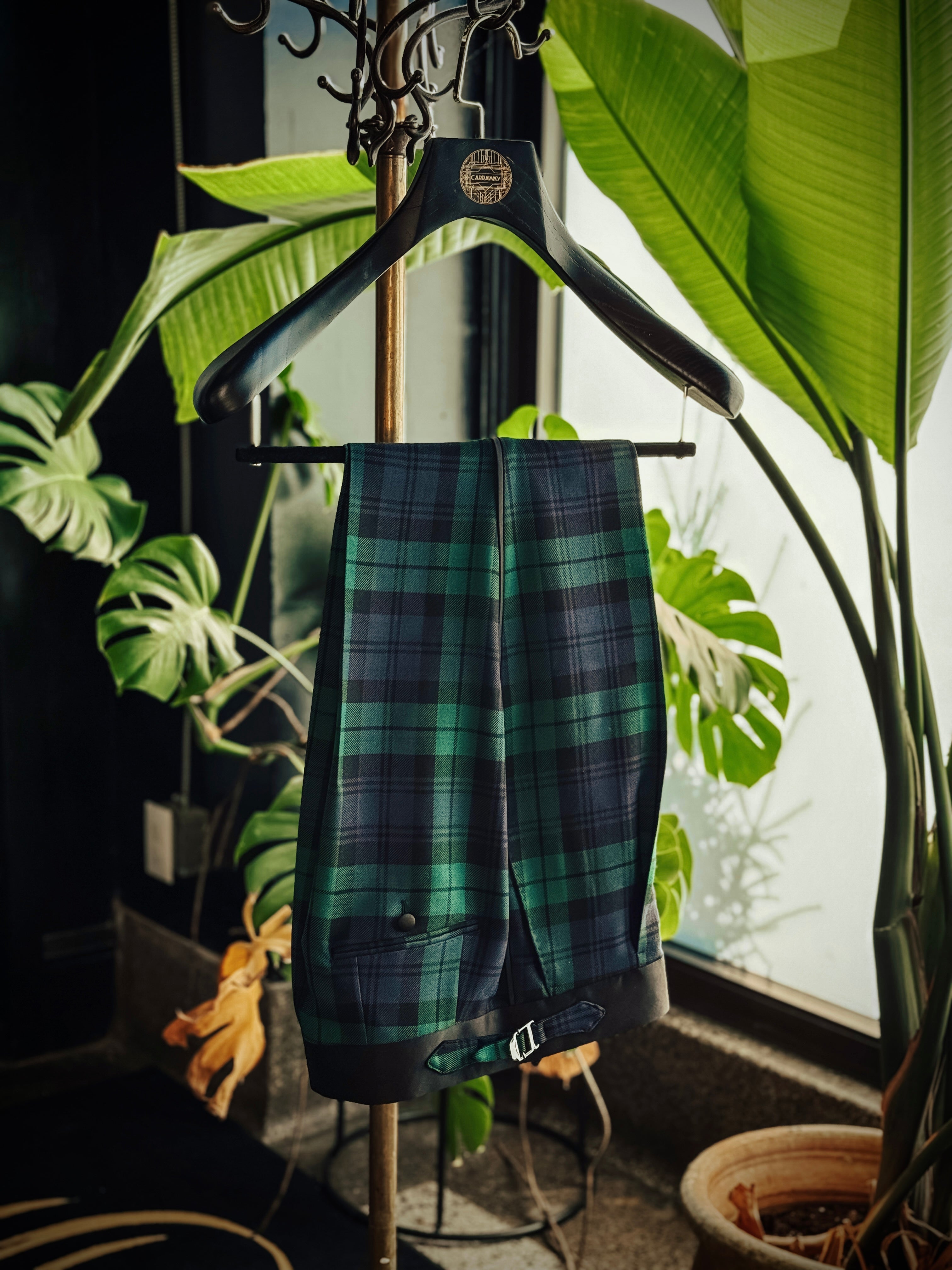 Plaid trouser hanging on a hanger with plants in the background